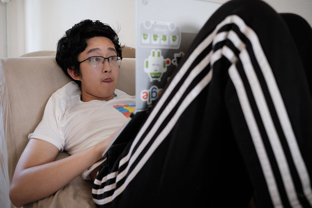 Portrait of a software engineer coding on the couch while laying down wearing Adidas 3-stripes jogging pants