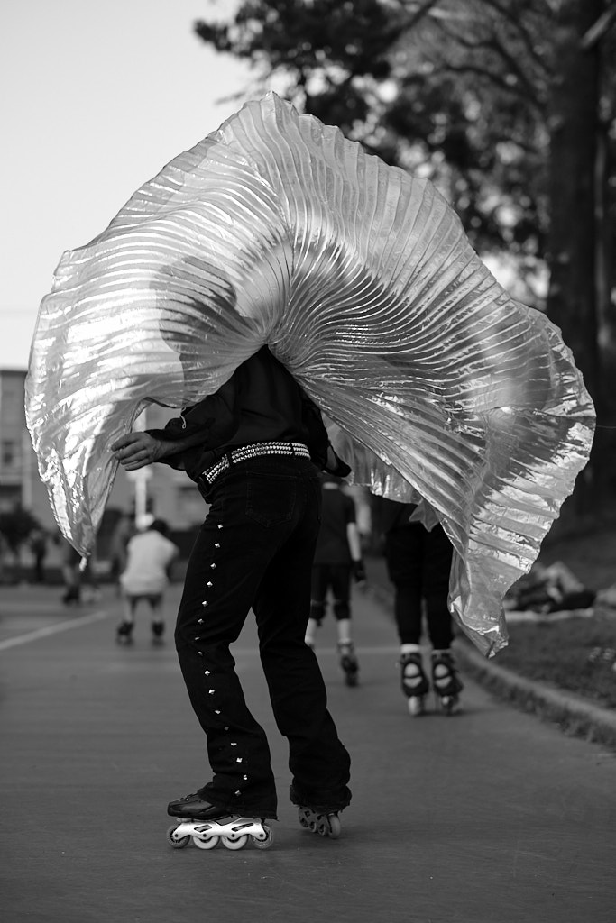 A man wearing disco-esque studded jeans flouting a shiny silver cape on rollerskates